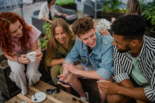 Four people sitting around a table looking at a cell phone.