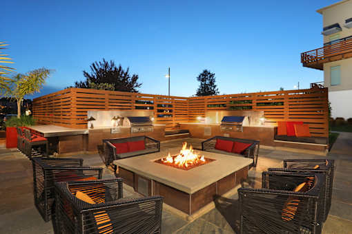 A patio with a fire pit surrounded by chairs.
