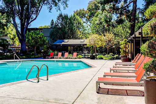 A pool with red chairs and a building in the background.