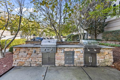 a stone barbecue area with two stainless steel appliances on the sidewalk