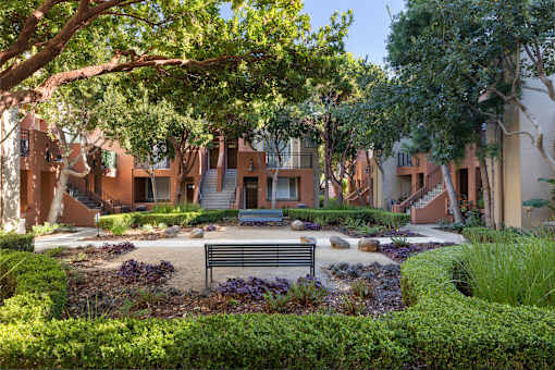 A bench is situated in the middle of a garden with a building in the background.