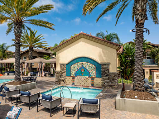 A pool area with a mosaic tile wall and lounge chairs.