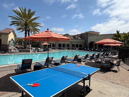 A blue table tennis table is in the middle of a poolside area.