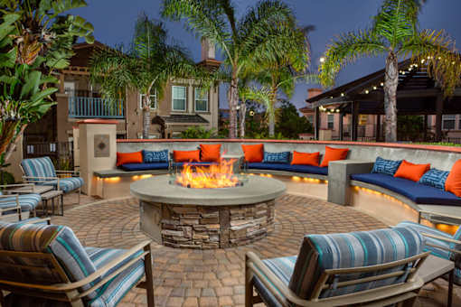 A fire pit in the middle of a patio surrounded by chairs and cushions.