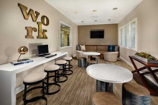 A room with a white desk and a white table with stools.