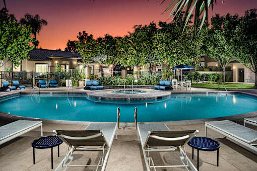 A pool surrounded by lounge chairs and umbrellas at dusk.