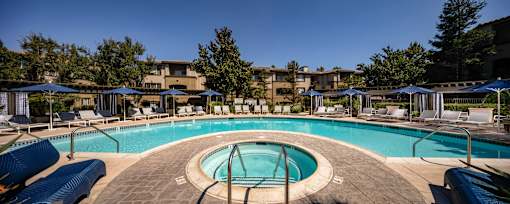 A large outdoor swimming pool surrounded by sun loungers and umbrellas.