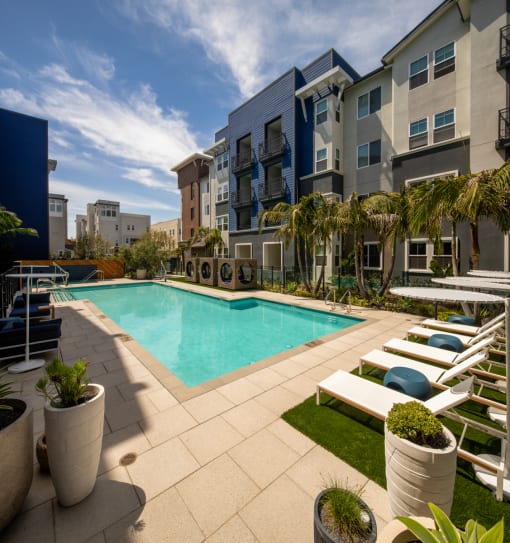 a swimming pool with lounge chairs and potted plants in front of an apartment building at Citron, Anaheim, 92805