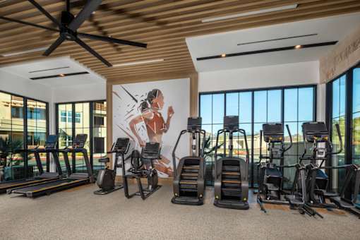 A gym with treadmills, exercise bikes, and a wall mural.
