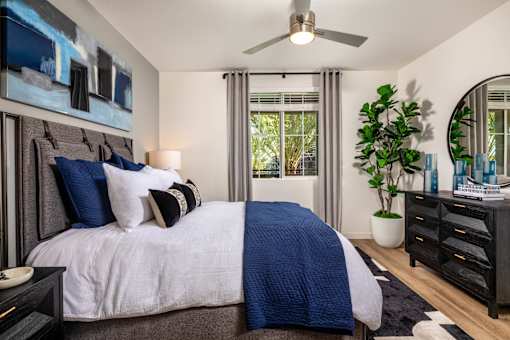 A bedroom with a bed, a ceiling fan, and a plant.