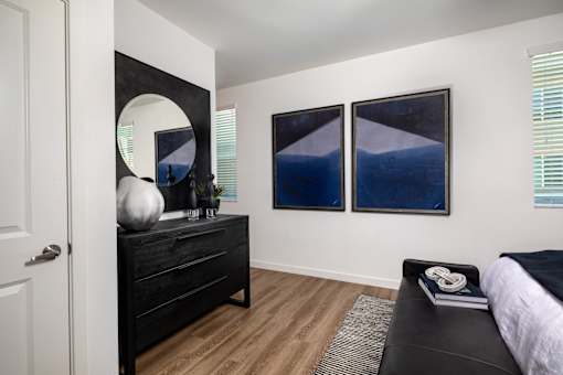 A bedroom with a black bed and a round mirror on the dresser.
