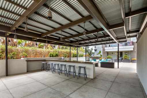 A patio with a bar and stools under a corrugated roof.