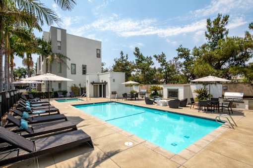 A pool area with lounge chairs and umbrellas in front of a white building.