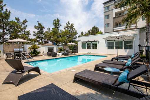 A pool with lounge chairs and umbrellas in front of a building.