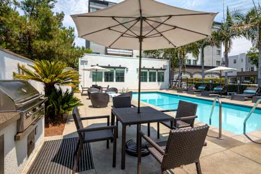 A patio with a table and chairs under an umbrella next to a pool.