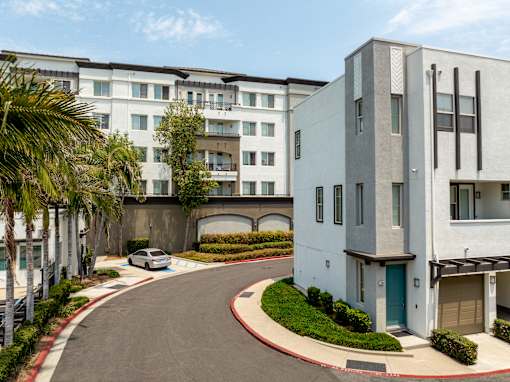 A white building with a blue door is situated on the right side of a curved driveway.