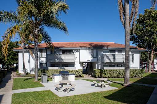 A white building with a red roof is surrounded by palm trees.