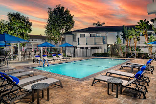A pool surrounded by chairs and umbrellas with a building in the background.