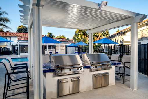 A barbecue grill is set up under a white pergola.