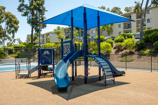 a playground with a blue slide and umbrella
