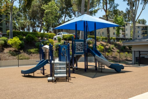 a playground with slides and a blue umbrella