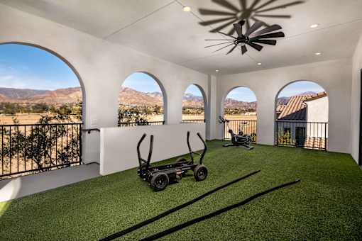 A black lawn mower is on a green lawn in a white room with arched windows at San Carlo Townhomes Apartments, Highland, California
