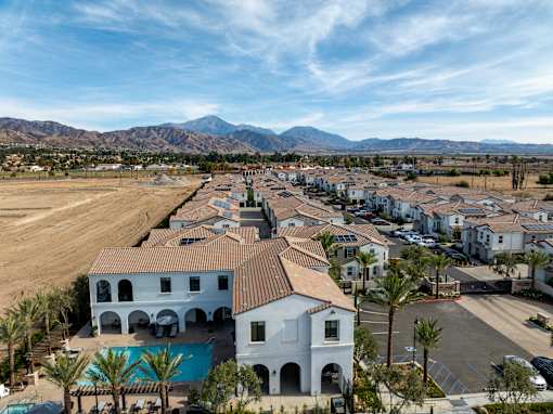 A white building with a red roof is surrounded by other buildings and palm trees at San Carlo Townhomes Apartments, Highland, CA
