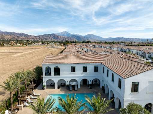 A large white building with a pool and palm trees in front at San Carlo Townhomes Apartments, Highland, 92346