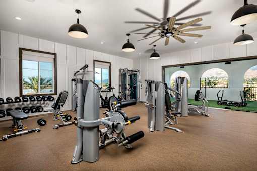 A spacious gym with a variety of equipment and a ceiling fan at San Carlo Townhomes Apartments, Highland, 92346