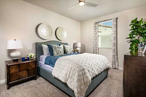 A bedroom with a bed, nightstand, and a plant at San Carlo Townhomes Apartments, California, 92346