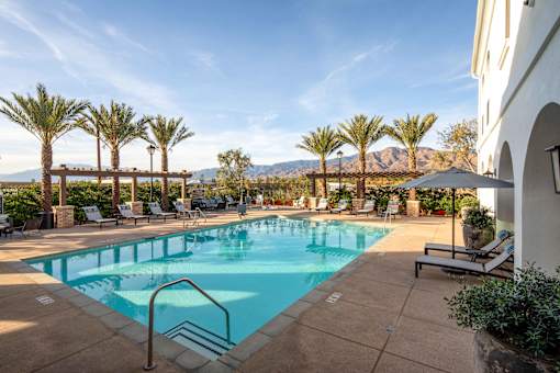 A pool surrounded by palm trees and lounge chairs at San Carlo Townhomes Apartments, California