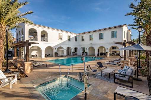 A large white building with a pool in front at San Carlo Townhomes Apartments, Highland, CA