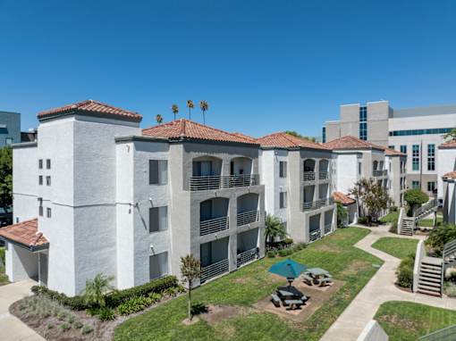 A white building with red tile roofs and a green lawn in front.