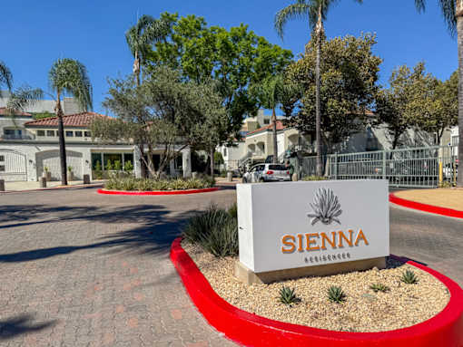 The image shows a sign for Sienna Residences in front of a gated community with palm trees and houses.
