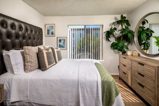 A bedroom with a large bed, a mirror, and a plant.