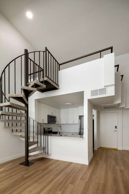 A spiral staircase with a metal railing and wooden steps leads to a kitchen area.