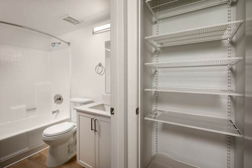 A white bathroom with a toilet, sink, and shelving unit.
