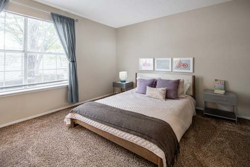 A bedroom with a large bed and a window with curtains.