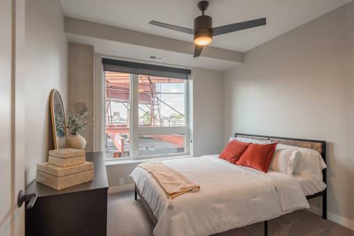 A bedroom with a bed, nightstand, and a window overlooking a building.