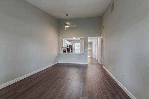 an empty living room with hardwood flooring and a hallway to a kitchen
