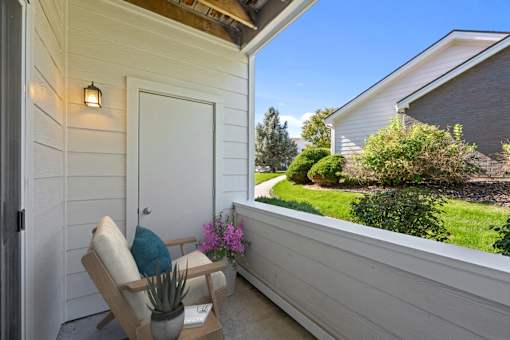 A chair with a cushion and a potted plant on a porch.