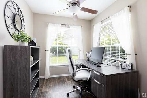 A room with a desk, chair, and a fan.