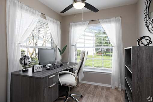 A home office with a desk, chair, and a fan.