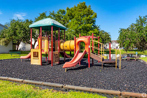A playground with a red and yellow slide and a green roofed structure.