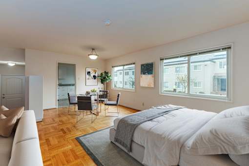 A bedroom with a large bed and a dining area in the background.
