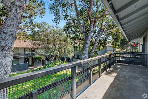 A balcony with a metal railing overlooks a green lawn and trees.
