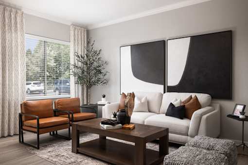 A living room with a white couch, a brown chair, a coffee table, and a large abstract painting on the wall.