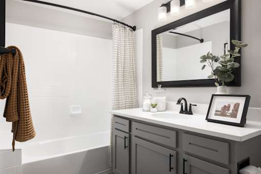 A bathroom with a white tub, a sink with a framed picture, and a towel hanging on the railing.