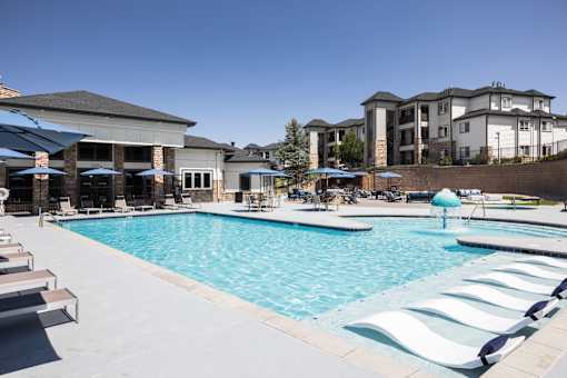 A large swimming pool with lounge chairs and umbrellas in front of a building.