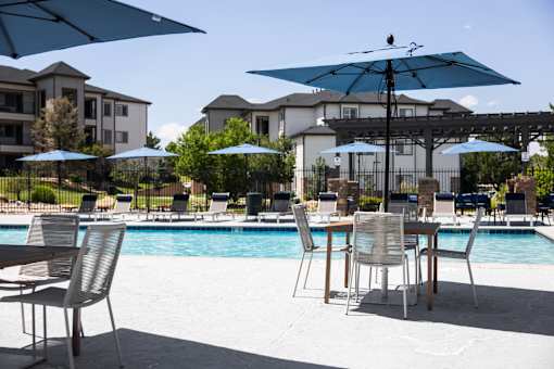 A poolside table with chairs and umbrellas is set up by the pool.